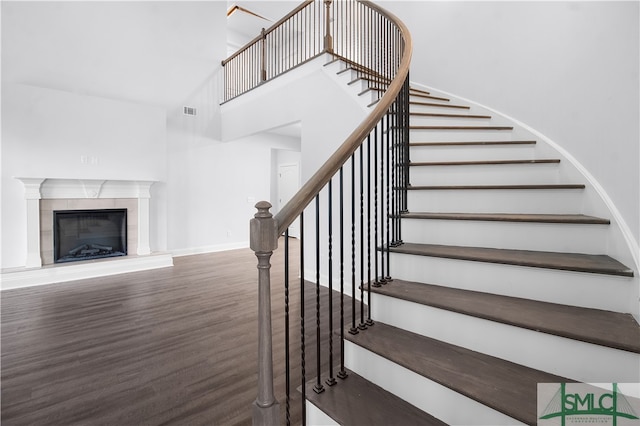 stairs with a high ceiling, a tile fireplace, and hardwood / wood-style flooring