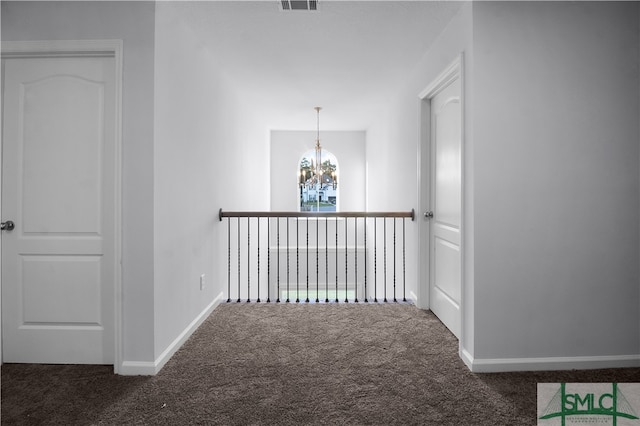 hall featuring dark colored carpet and a notable chandelier