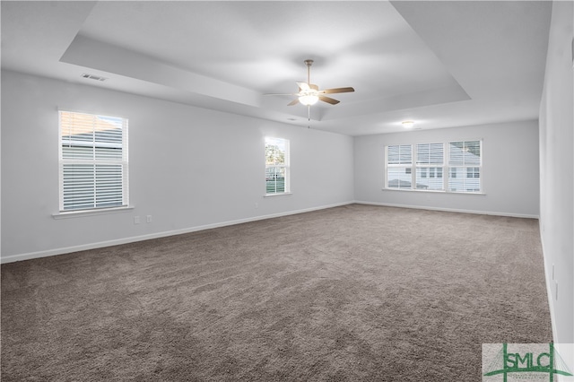 empty room with ceiling fan, a tray ceiling, and carpet