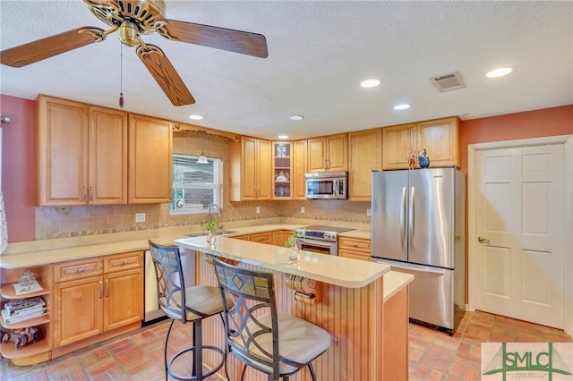 kitchen with ceiling fan, decorative backsplash, a breakfast bar area, and appliances with stainless steel finishes