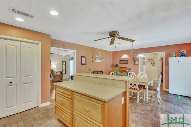 kitchen with white refrigerator, ceiling fan, a textured ceiling, light brown cabinetry, and decorative light fixtures