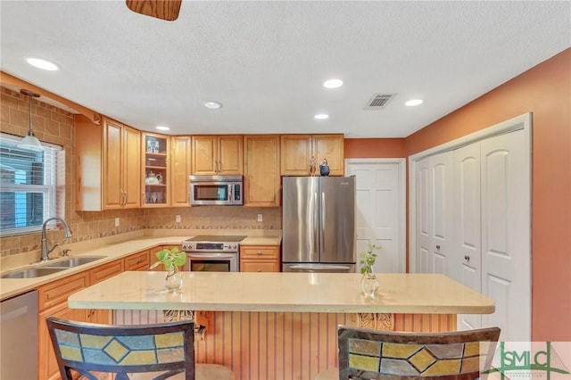 kitchen featuring a kitchen breakfast bar, backsplash, a textured ceiling, stainless steel appliances, and sink