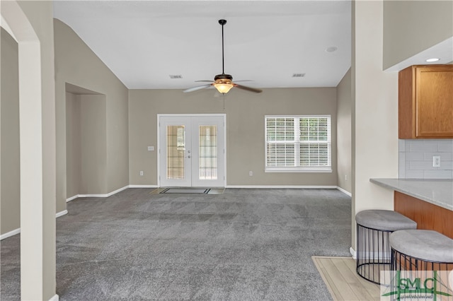 unfurnished living room with carpet floors, ceiling fan, vaulted ceiling, and french doors