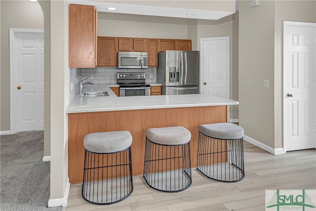 kitchen with backsplash, sink, a kitchen bar, light hardwood / wood-style flooring, and stainless steel appliances