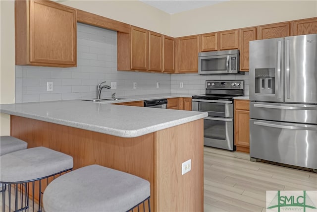 kitchen featuring stainless steel appliances, light hardwood / wood-style flooring, tasteful backsplash, sink, and a breakfast bar