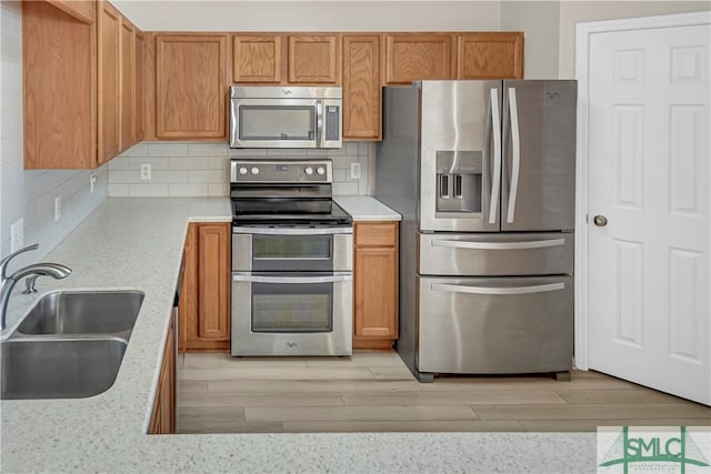 kitchen with sink, stainless steel appliances, light hardwood / wood-style flooring, and decorative backsplash