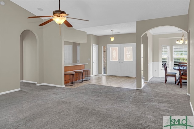 entrance foyer with ceiling fan with notable chandelier, french doors, and light carpet