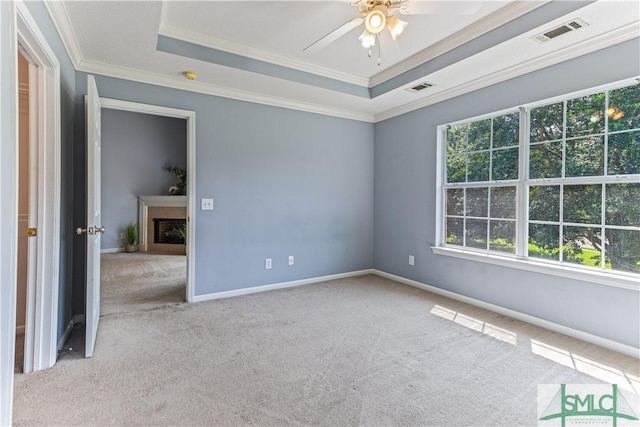 unfurnished room featuring a tray ceiling, a fireplace, visible vents, and crown molding