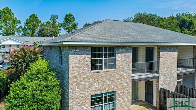 exterior space with brick siding, a shingled roof, and a balcony