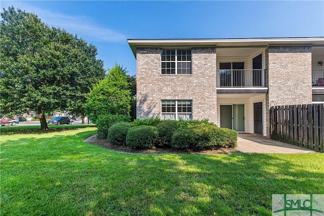 view of front of property featuring a patio, brick siding, a front lawn, and fence