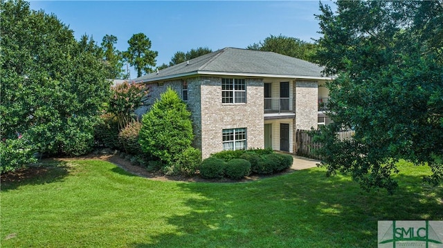 exterior space featuring brick siding, a front yard, fence, and a balcony