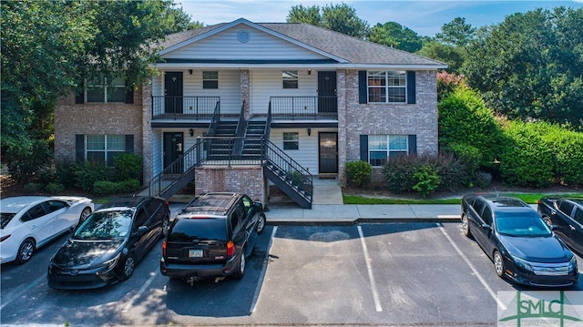 view of front of home with uncovered parking, brick siding, a shingled roof, and stairs