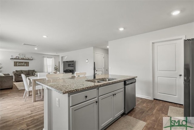 kitchen with a kitchen island with sink, stainless steel appliances, a sink, open floor plan, and dark wood-style floors