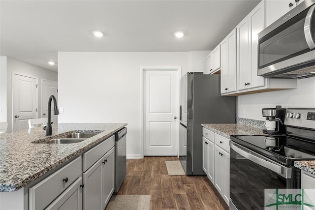 kitchen with dark wood-type flooring, appliances with stainless steel finishes, light stone counters, and a sink