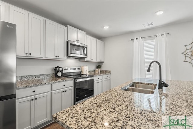 kitchen with light stone counters, a sink, visible vents, white cabinetry, and appliances with stainless steel finishes