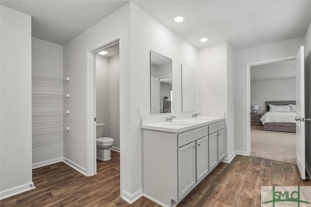 ensuite bathroom featuring double vanity, toilet, baseboards, and wood finished floors