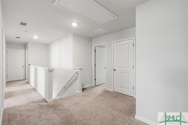 hall featuring light carpet, attic access, visible vents, baseboards, and an upstairs landing