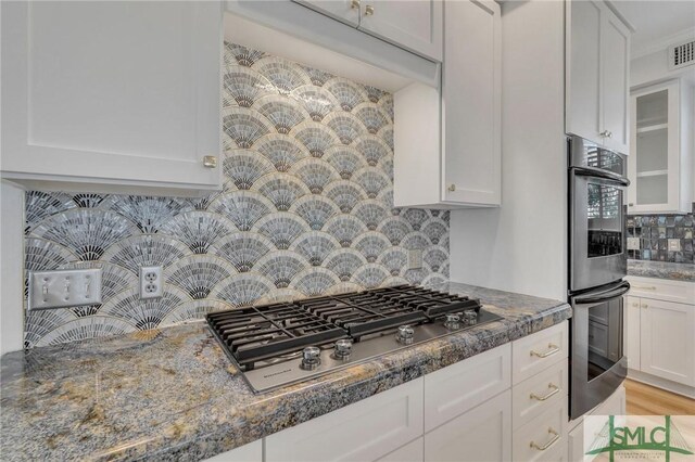 kitchen featuring backsplash, light hardwood / wood-style flooring, stainless steel appliances, white cabinetry, and dark stone counters