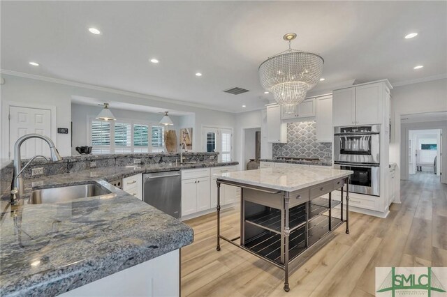 kitchen featuring light wood-type flooring, stainless steel appliances, sink, dark stone counters, and pendant lighting