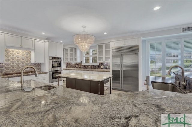 kitchen with pendant lighting, backsplash, stainless steel appliances, sink, and white cabinetry