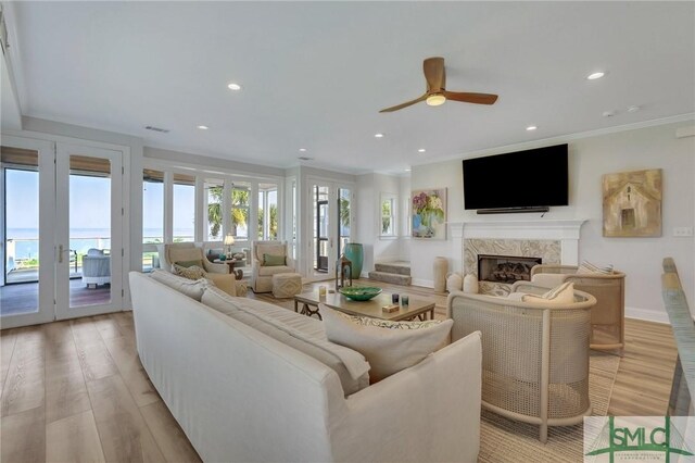 living room featuring light hardwood / wood-style flooring, a healthy amount of sunlight, a high end fireplace, and ceiling fan