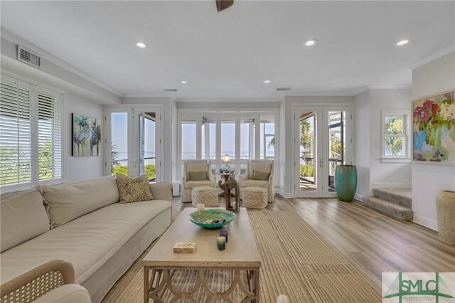 living room featuring light wood-type flooring, french doors, crown molding, and plenty of natural light