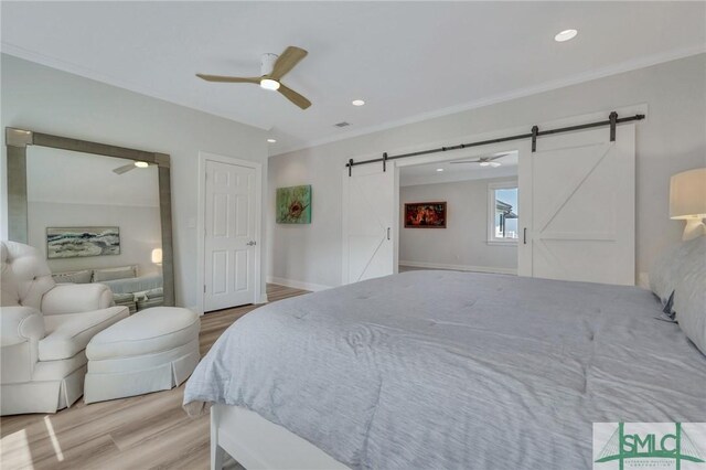 bedroom with a barn door, ceiling fan, wood-type flooring, and ornamental molding