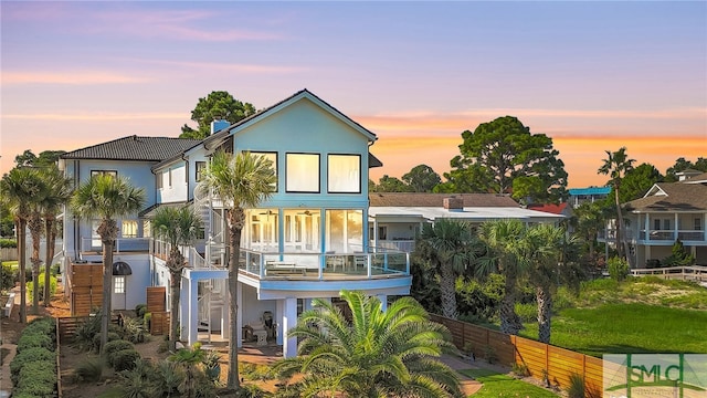 back house at dusk featuring a balcony and a lawn