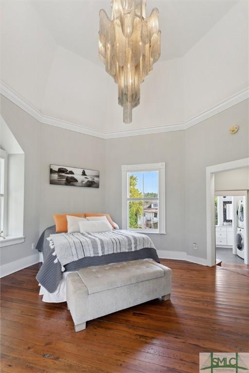 bedroom with stacked washing maching and dryer, a chandelier, ornamental molding, and wood-type flooring