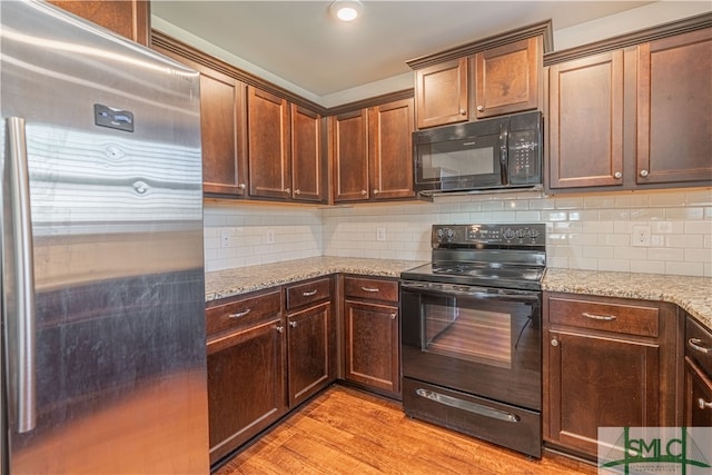 kitchen featuring light hardwood / wood-style flooring, decorative backsplash, black appliances, and light stone counters