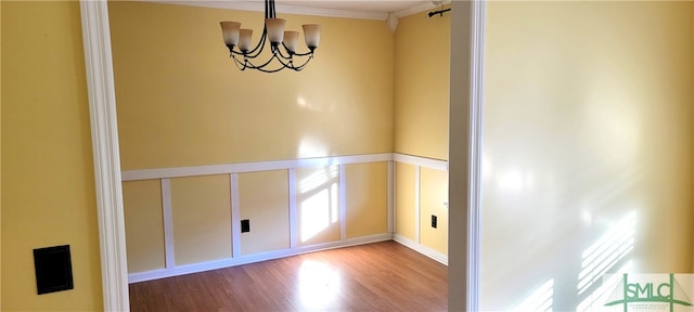 empty room with hardwood / wood-style flooring, ornamental molding, and an inviting chandelier