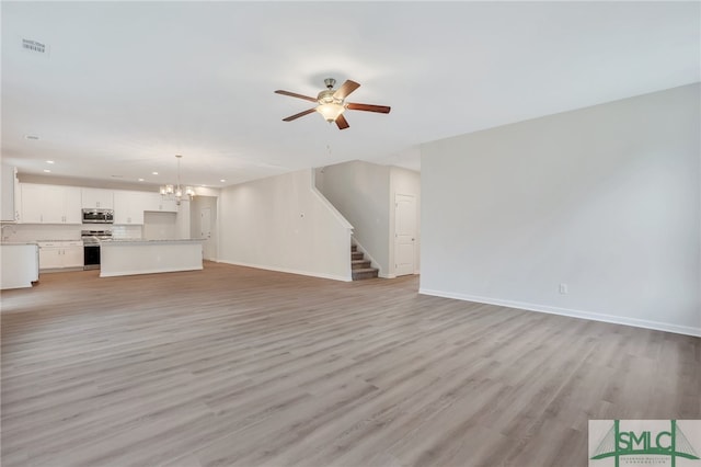 unfurnished living room with ceiling fan with notable chandelier and light hardwood / wood-style floors