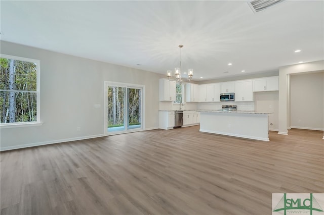 kitchen with a kitchen island, pendant lighting, a wealth of natural light, white cabinetry, and appliances with stainless steel finishes