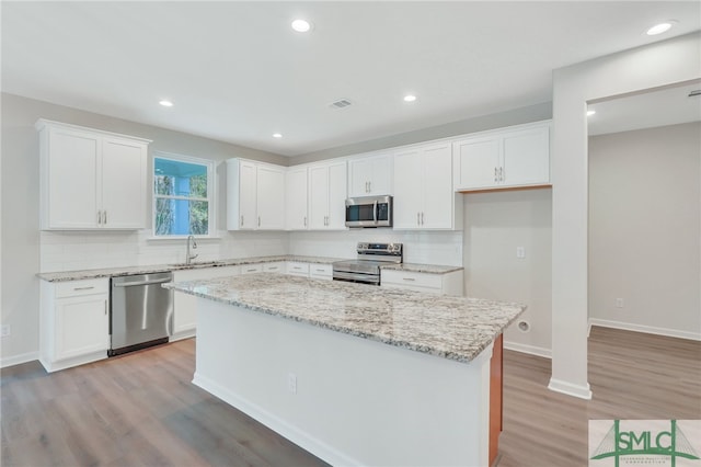 kitchen with a center island, sink, stainless steel appliances, white cabinets, and light stone counters