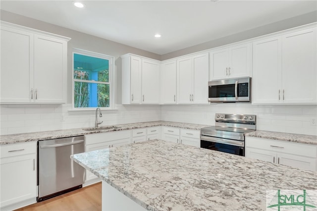 kitchen with sink, light stone counters, stainless steel appliances, and white cabinetry