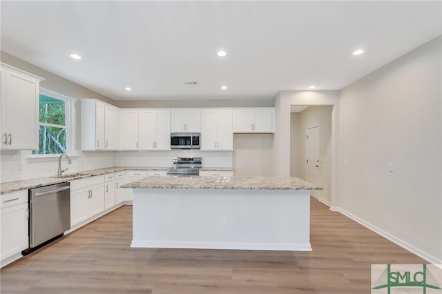 kitchen featuring a center island, light wood-type flooring, stainless steel appliances, white cabinets, and light stone counters