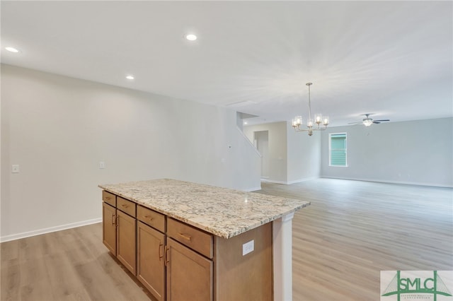 kitchen featuring light wood-type flooring, hanging light fixtures, light stone countertops, ceiling fan with notable chandelier, and a center island