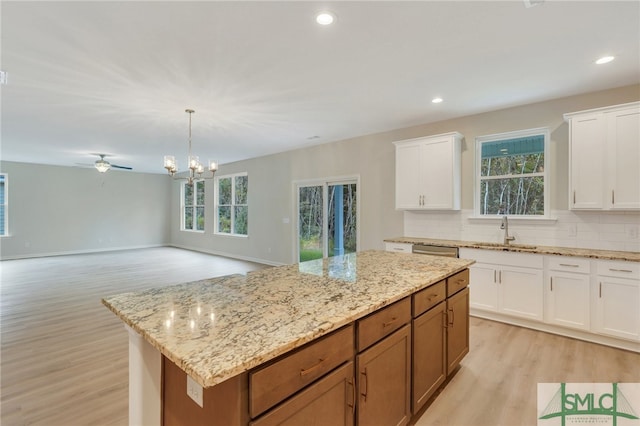 kitchen with ceiling fan with notable chandelier, a center island, white cabinetry, tasteful backsplash, and light wood-type flooring