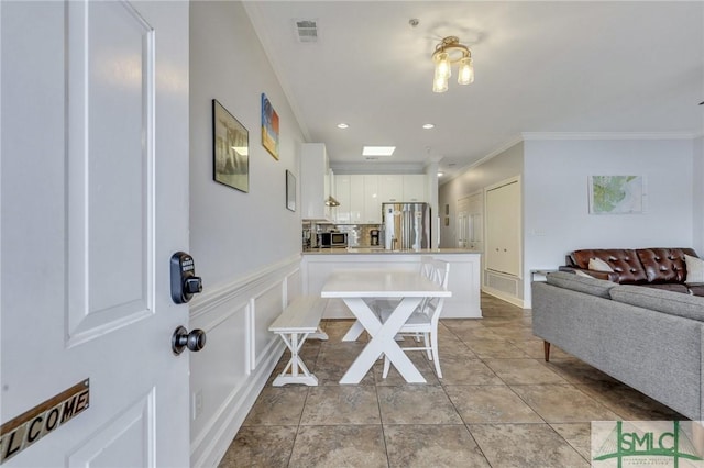 kitchen featuring appliances with stainless steel finishes, light tile patterned flooring, crown molding, white cabinetry, and a kitchen bar