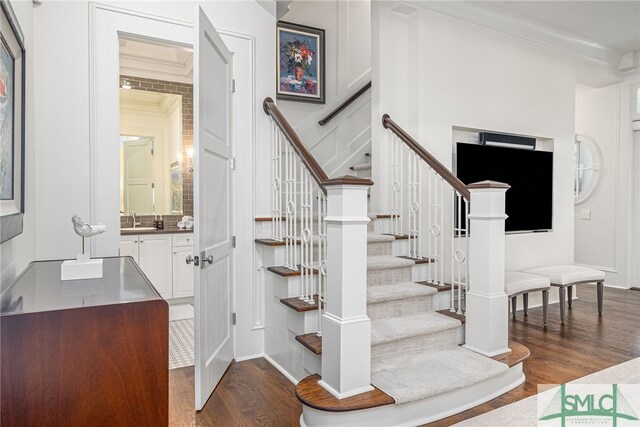 staircase with hardwood / wood-style floors, ornamental molding, and sink