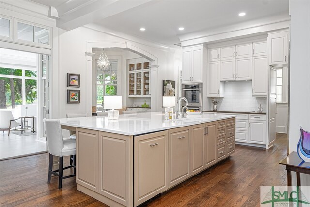 kitchen featuring white cabinets, a kitchen island with sink, a wealth of natural light, and dark wood-type flooring