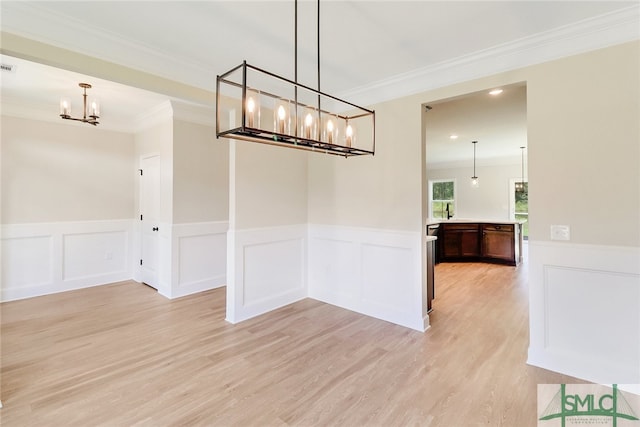 unfurnished dining area featuring light wood-type flooring, crown molding, and a notable chandelier