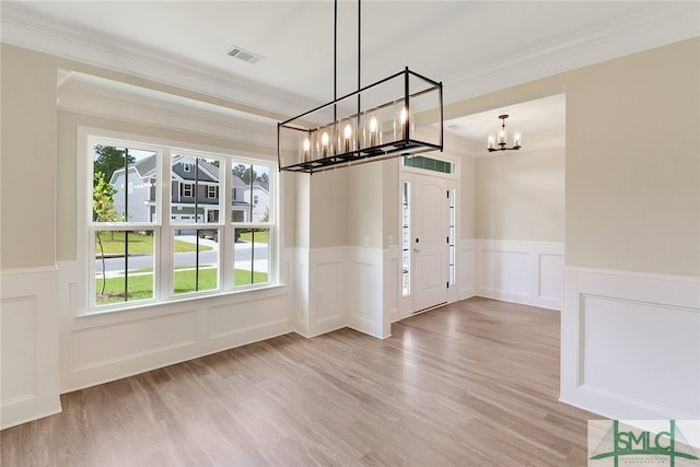 unfurnished dining area featuring light hardwood / wood-style flooring, ornamental molding, and a chandelier