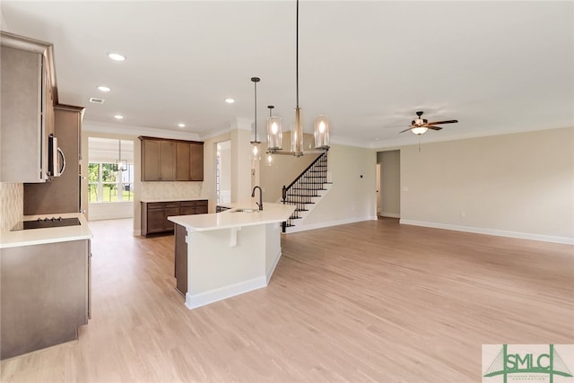 kitchen featuring sink, light wood-type flooring, ceiling fan with notable chandelier, pendant lighting, and a center island with sink