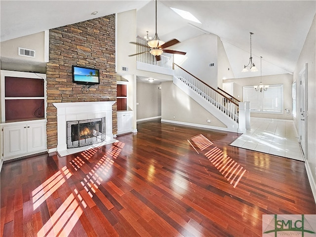 unfurnished living room with high vaulted ceiling, built in shelves, a stone fireplace, and wood-type flooring