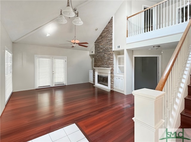 unfurnished living room with a stone fireplace, high vaulted ceiling, ceiling fan with notable chandelier, plenty of natural light, and hardwood / wood-style flooring