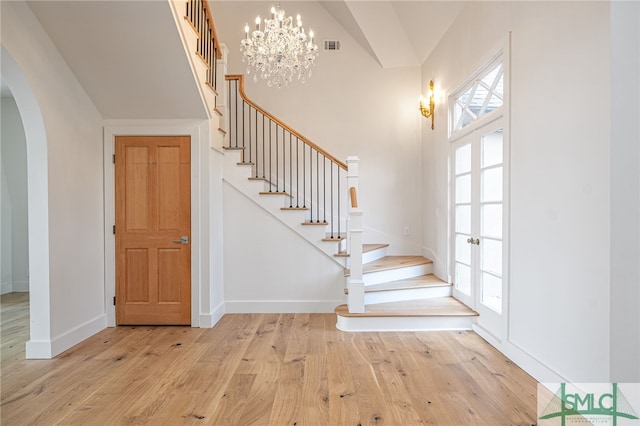 entrance foyer featuring arched walkways, light wood finished floors, visible vents, stairway, and baseboards