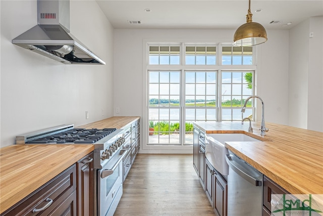 kitchen with light wood finished floors, stainless steel appliances, visible vents, wood counters, and wall chimney exhaust hood