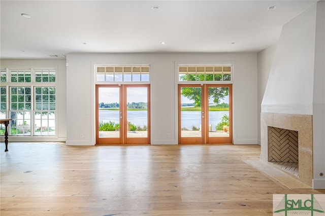 unfurnished living room featuring french doors, a water view, a high end fireplace, light wood-type flooring, and baseboards