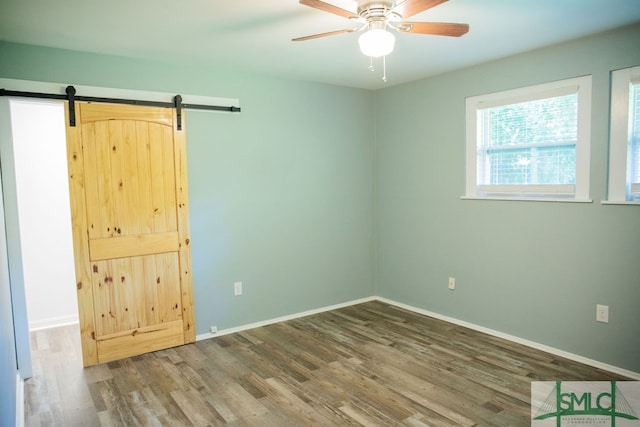 unfurnished room with ceiling fan, wood-type flooring, and a barn door